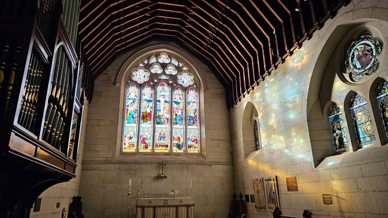 Sunlight filters through colorful stained glass windows in a church, casting vibrant patterns on the stone walls. Like high Local SEO ranking, the wooden ceiling arches overhead, drawing eyes toward the candle-lit altar below the main window.